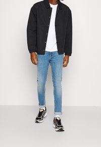 Czarna kurtka zapinana na guziki na białej koszulce, jasnoniebieskie obcisłe jeansy i czarne sneakersy z srebrnymi akcentami. Codzienny strój z wyraźnie zaznaczonymi warstwami.