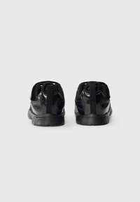 Sapatos atléticos pretos com parte superior em malha texturizada e sobreposições de nylon, apresentando um colar acolchoado e sola de borracha durável, vistos de trás.