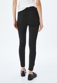 Svarta skinny jeans med ett slätt, elastiskt tyg, med två bakfickor, hög midja och slim fit-design, bärs med svarta skor.