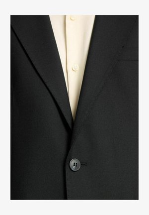 Svart skräddarsydd kavaj med struktur, med en enkel knappstängning och en ljus skjorta med synliga knappar.
