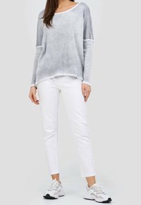 Ljust grå långärmad topp med rundad halsringning, bärs med vita slim-fit byxor och vita sneakers med svarta detaljer.