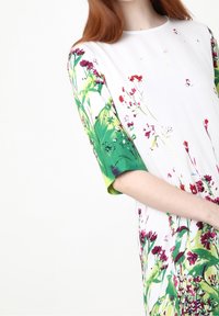 Vestido floral con un cuerpo blanco y mangas verdes, adornado con estampados botánicos en tonos rosa y verde. Tejido suave con un corte holgado.
