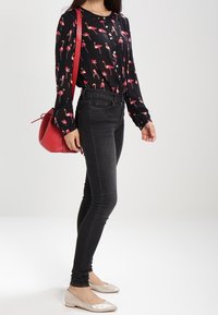Schwarzes Langarmshirt mit einem Flamingo-Print, kombiniert mit schwarzen Skinny-Jeans und silbernen Ballerinas. Eine rote Tasche hängt über einer Schulter.