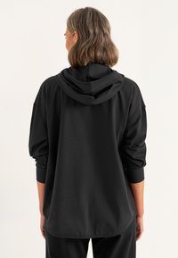 Zwarte hoodie met een relaxte pasvorm, zachte textuur, drop shoulders en ribgebreide mouwen. Bevat een kangoeroezak aan de voorkant.