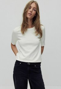 Hvid t-shirt med korte ærmer og rund halsudskæring, lavet af blødt materiale, parret med mørke denim jeans med bælte og lommer.