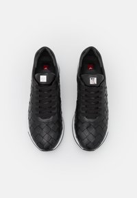 Svarta sneakers med vävt läderöverdel, rund tå, vit gummisula, sex svarta snörningar och en metallisk logotag på tungan.