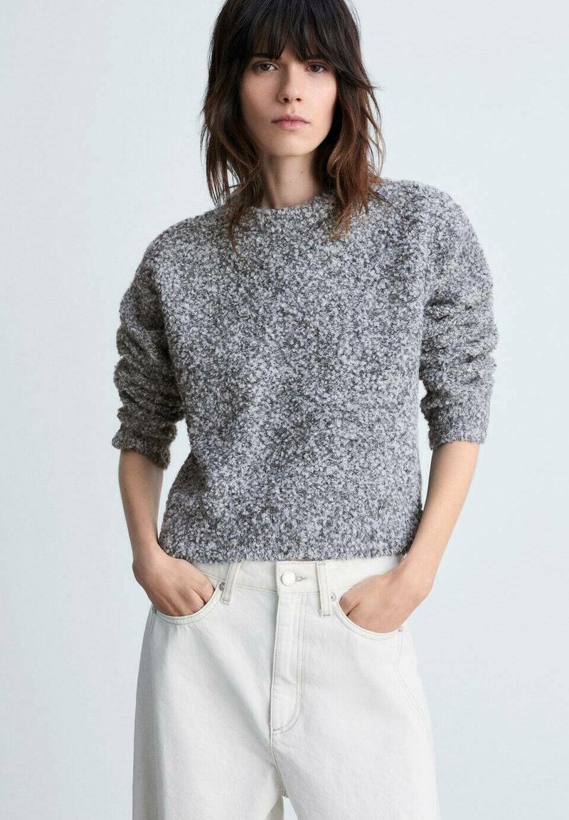 Maglione grigio texturizzato con maniche lunghe e scollo a girocollo, abbinato a pantaloni a vita alta di colore chiaro. Nessun motivo o materiale hardware visibile.