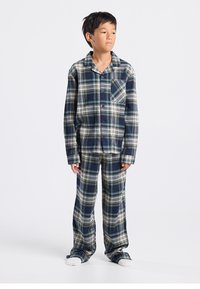 Geruit flanellen pyjamaset in marineblauw, groen en wit. Overhemd met knoopsluiting en een borstzak, loszittende broek en zachte witte zolen.