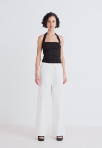 Black fitted halter top paired with loose, white wide-leg trousers and chunky black platform shoes on a neutral background.