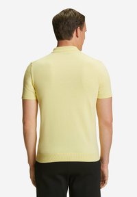 Polo a maniche corte in morbido tessuto a maglia giallo chiaro. Presenta un colletto e un orlo a costine, con cuciture pulite e una silhouette aderente.