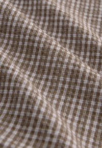 Tela de cuadros marrón y blanca con una textura suave, que presenta un patrón de cuadrícula y sutiles variaciones en la intensidad del color.