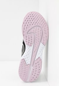 Semelle de chaussure de sport noire avec un motif ondulé rose et blanc, comportant des textures de grip et des accents circulaires pour l'adhérence.