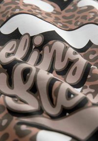 Textiel met een luipaardprint in bruin- en zwarttonen, voorzien van gedurfde, gestileerde tekst in crèmekleurige en roze tinten. Het oppervlak heeft een gladde textuur.