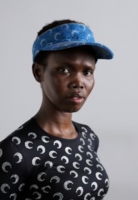 Blue fabric visor with a wave pattern, complemented by a fitted black shirt featuring metallic crescent shapes. Smooth texture, sleek design.