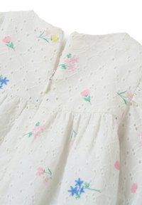 Abito bianco in tessuto ricamato con motivi floreali in rosa, blu e giallo, dotato di un motivo traforato testurizzato e chiusura con zip sulla schiena.