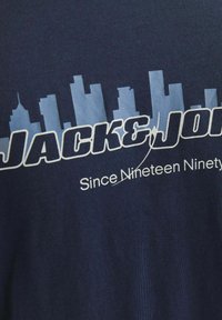 Tamsiai mėlynas medvilnės marškinėliai su miesto vaizdu šviesiai mėlyna spalva ir balta tekstu: "JACK&JONES" ir "Nuo devyniolikto amžiaus devintojo mėnesio."