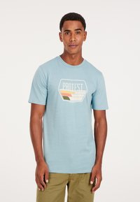 Camiseta de manga corta azul claro hecha de algodón, que presenta un logo gráfico en blanco, naranja, amarillo y verde en el frente.