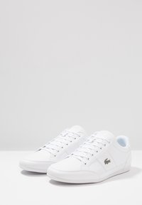 Baskets basses blanches en matériau synthétique lisse, avec un design à lacets, un embout arrondi et un subtil accent de logo.