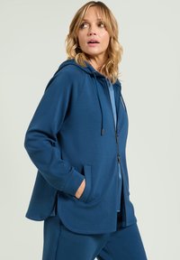 Felpa blu con zip, coulisse, tasche frontali e polsini a costine. Tessuto morbido con una superficie liscia e orlo curvo.