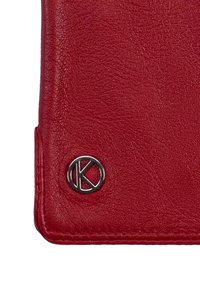 Czerwony portfel ze skóry posiadający teksturowaną powierzchnię, obszyte brzegi oraz metaliczne, okrągłe logo z literą „K” w rogu.