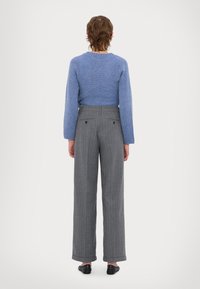 Maglione blu a maglia con collo rotondo, abbinato a pantaloni larghi a righe grigie con tasche posteriori. Texture dei tessuti lisci visibili.