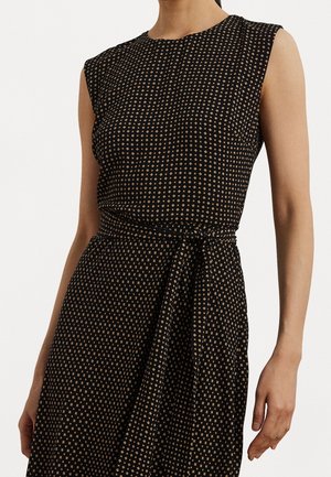 Bezrekawowa czarna sukienka z drobnym beżowym wzorem geometrycznym i wiązanym paskiem w talii, noszona przez stojącą osobę.