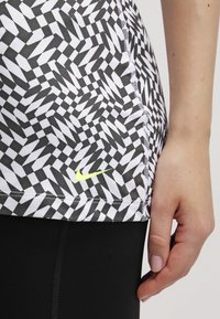 Korte mouw top in een geometrisch zwart-wit patroon met een gele Nike-logo, voorzien van een afgeronde zoom en gedetailleerde stiksels.