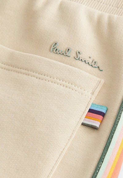 Beige szövet, látható textúrával. A „Paul Smith” logó teal színben, egy zseb és sokszínű csíkos címkék találhatóak az oldalon.
