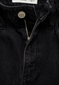 Mustat farkut, joissa on metallinen napitus, vetoketjuhaitari ja sivutaskut, joissa on hieman teksturoitu kangas.