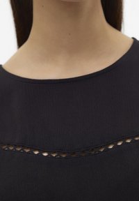 Haut bleu marine foncé avec un décolleté arrondi, en tissu texturé et un détail découpé décoratif au niveau de la poitrine.