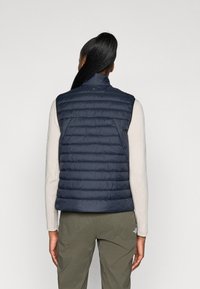 Colete isolante azul-marinho com gola alta, apresentando um design acolchoado e uma textura suave. A vista traseira mostra uma silhueta ajustada.