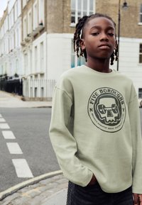 Šviesiai žalias ilgomis rankovėmis džemperis su tekstūruota medžiaga, centre juodas grafikos atvaizdas - kaukolė su svarmenimis ir tekstu „FIVE BOROUGHS“.