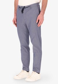 Pantaloni leggeri blu chiaro da uomo con finitura testurizzata, dotati di vita con cordoncino e tasche laterali, abbinati a sneaker bianche.