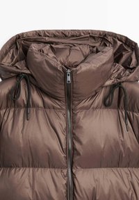 Giacca imbottita marrone con colletto alto, zip frontale, cappuccio attaccato e cordini neri su ciascun lato del cappuccio.