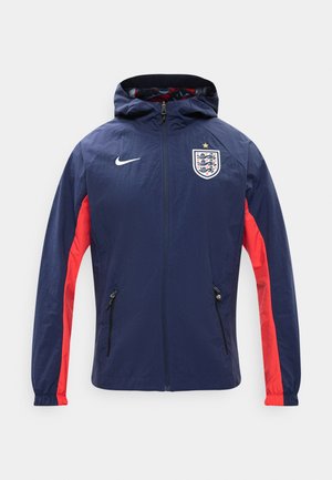 Σκούρο μπλε μπουφάν με κουκούλα και κόκκινα πλαϊνά πάνελ, τσέπες με φερμουάρ, το έμβλημα της ποδοσφαιρικής ομάδας της Αγγλίας με ένα αστέρι και λευκό λογότυπο Nike στο στήθος.
