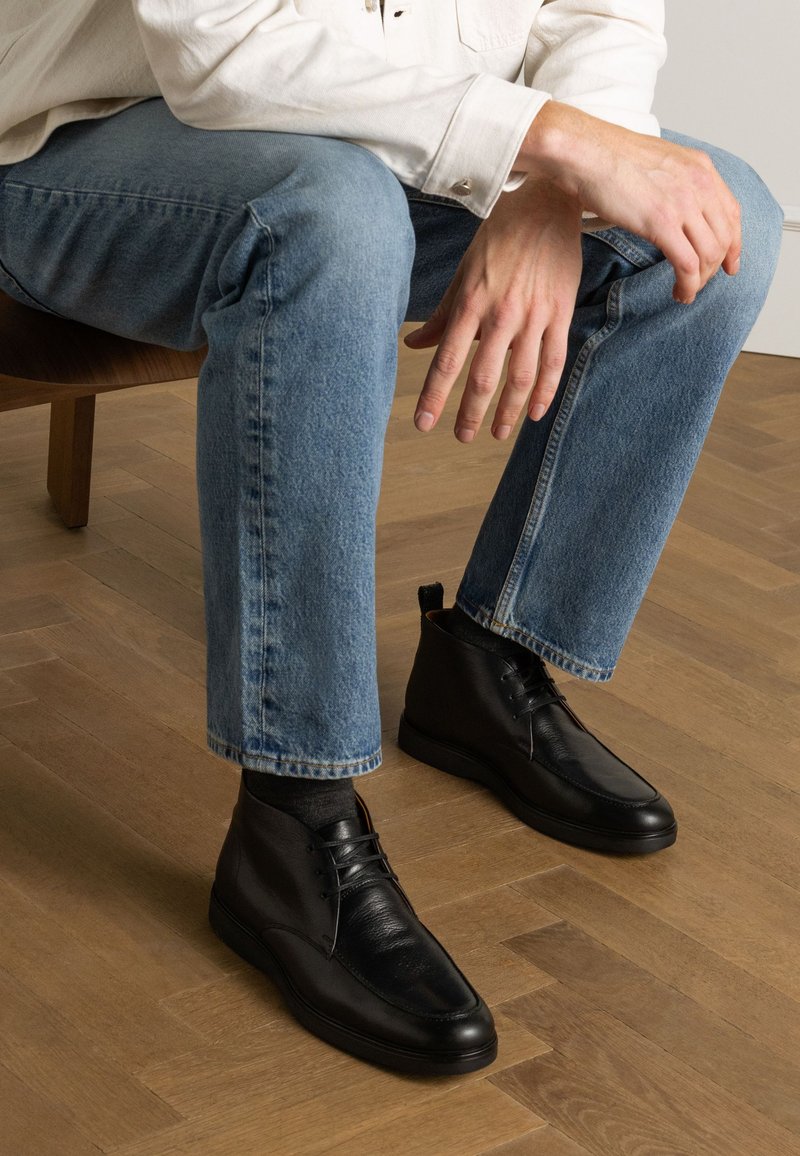 Bottines noires en cuir avec une finition lisse, dotées d'un laçage et d'une semelle rembourrée, portées avec un jean en denim bleu clair.