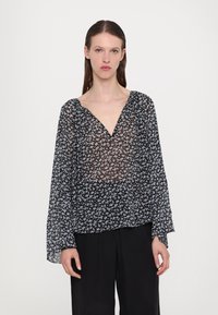 Blouse noire transparente avec un petit motif floral bleu, décolleté en v et manches longues. Tissu doux et léger avec une coupe ample.