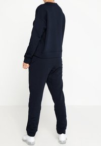Felpa blu navy e pantaloni abbinati realizzati in morbido tessuto. Vestibilità rilassata con polsini e vita a coste, design minimalista.