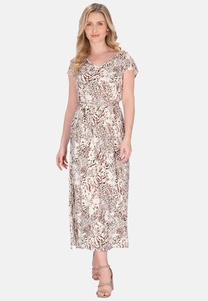 Kobieta ubranа w beżowo-brązową maxi sukienkę na krótki rękaw w zwierzęcy wzór, z paskiem w talii, stoi i uśmiecha się, nosi beżowe sandały na słupku.