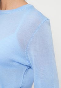 Γαλάζια μπλούζα μακρυμάνικη από μαλακό, ελαφρύ ύφασμα. Διαθέτει στρογγυλεμένο λαιμόκοψη και διακριτική υφή με ορατές ραφές.