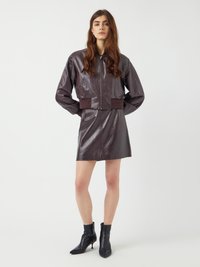 Bordeaux leren bomberjack met een cropped ontwerp, gecombineerd met een bijpassende leren minirok. Zwarte enkellaarsjes maken de look af.