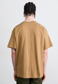 Tricou scurt maro din bumbac, cu un croi lejer și un finisaj curat, fără logo-uri sau modele vizibile.