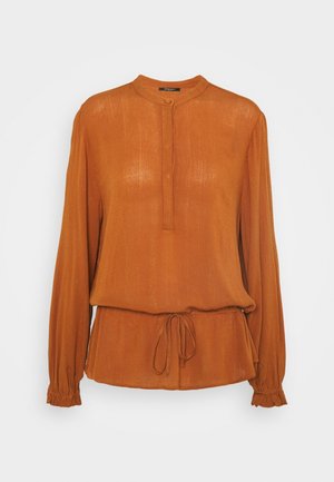 Blouse à manches longues couleur rouille avec petit col montant, patte de boutonnage, taille à cordon de serrage et poignets élastiques.