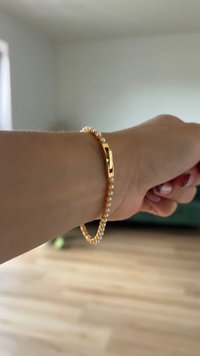 Zeltīts rokassprādze ar pārmaiņus izvietotām mazām baltām pērļu pērlītēm, ar ģeometrisku aizdari. Dizains ir elegants, ar pulētu apdari un gludu tekstūru.