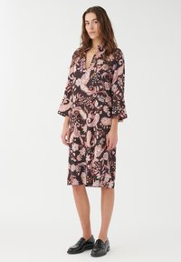 Svart klänning med ett blommigt paisley-mönster i rosa och krämfärg. Har en notch-krage, trekvartslånga klockärmar och en rak skärning.
