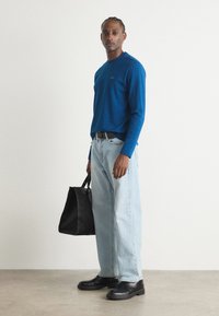 Blå langermet skjorte med rund hals, lyse vaskede baggy-jeans, svarte sko og en svart strukturert totebag.