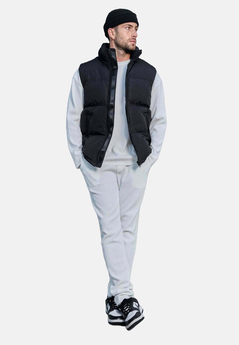 Doudoune noire avec col montant superposée à un sweat-shirt gris clair et un pantalon assorti. Baskets noires et blanches avec texture rayée visible.