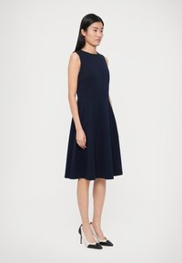 Námornícka A-líniová sukňa z hladkej látky s priliehavým živôtikom a rozšírenou sukňou. Kombinovaná s čierno-bielymi lodičkami s špicatou špičkou.