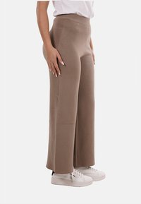Pantaloni ampi a vita alta, lavorati a maglia, di colore marrone chiaro. Texture morbida con una finitura liscia, abbinati a sneakers platform bianche.