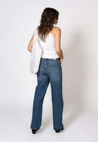 Hvit tank topp med rosa kant, blå høyt liv rette jeans, og en hvit blonde tote bag, svarte sko, bølgete hår.